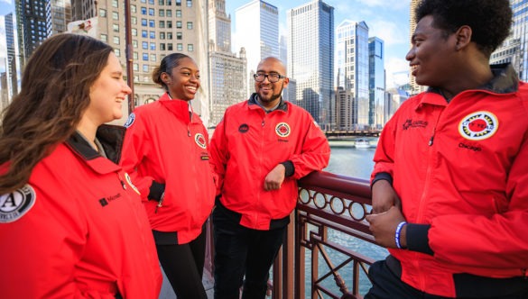 A group of AmeriCorps members are gathered on a walking bridge in the city.