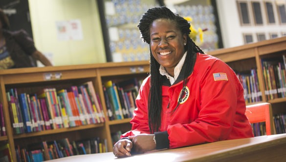 An AmeriCorps member sits at a table in a school library.