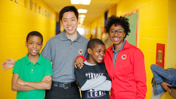 Two city year americorps members posing with two young students in a school hallway.