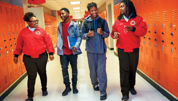 two AmeriCorps members are walking and talking with two high school students in the hallway