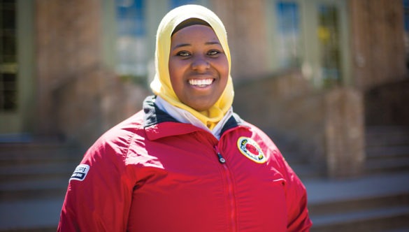 AmeriCorps member stands in by the front steps on a school building and smiles..