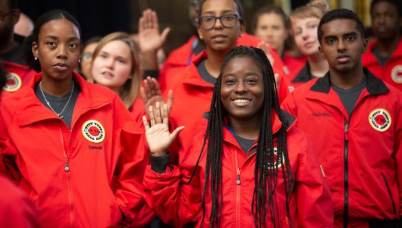 A cohort of City Year AmeriCorps members raise their right hand as they say the City Year pledge