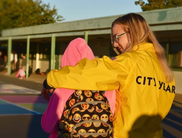 An AmeriCorps member waking into school with a student with an emoji backpack
