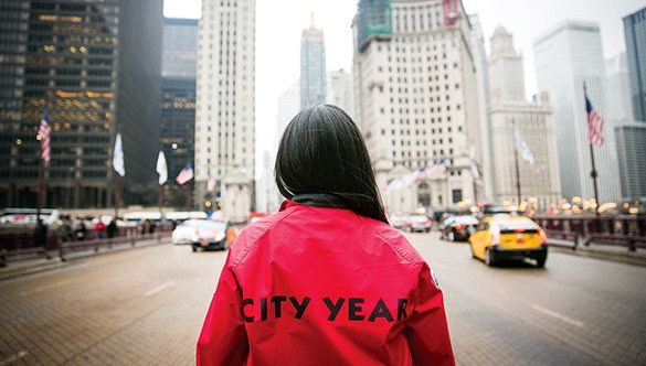 City Year AmeriCorp Member with their back towards the camera facing a large cityscape