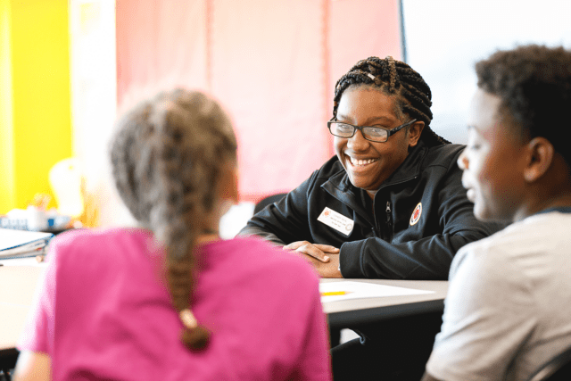 A City Year Buffalo AmeriCorps member laughs and looks across the table at two students