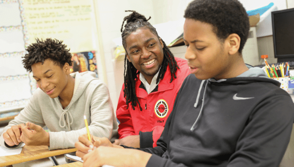 City Year AmeriCorps member helping two students at their desks