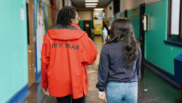 A City Year AmeriCorps member and student walk down a school hallway