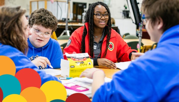 Photo of AmeriCorps member with three students at a table engaged in a project, with a graphic of colorful balloon-like shapes overlayed in one corner